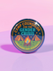 Round glossy pinback button measuring 2.25 inches featuring a playful camp-themed design with the phrase “Camp Counselor for the Gender Crisis.” The artwork includes two orange tents, a rainbow campfire, stars, and green grass. Bottom text reads “Cabin Queer, Unit Psychedelic.” Made from durable tinplate with a safety pin back and coated in a UV and scratch-resistant mylar finish. Bold and colorful, perfect for jackets, bags, or pride outfits.