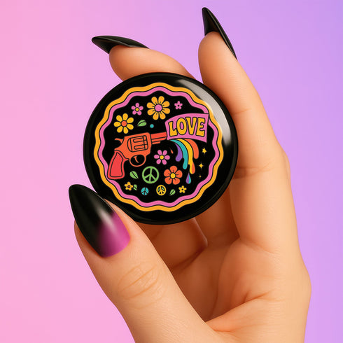 Round pinback button badge with a black background, featuring a retro illustration of a red revolver shooting out a rainbow flag that says “LOVE.” Surrounded by colorful 70s-style flowers and peace signs, outlined in wavy neon border. Glossy finish with vibrant pop colors and psychedelic design.