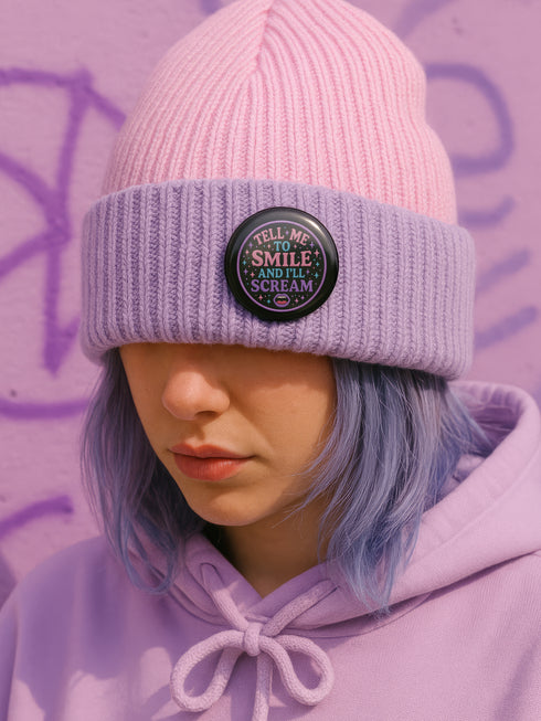 Glossy black pinback button with pastel-colored embroidered-style text that reads “Tell Me to Smile and I’ll Scream,” with lips icon and star accents.