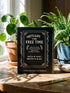 An 8.5 x 11 inch black hardcover spiral planner with a durable satin matte laminated finish. The front cover features a vintage-style white ornamental border, creating a gothic, macabre aesthetic. Inside the frame, the title "Calendar of Doom" is printed in an antique serif font. This undated weekly and monthly agenda is shown with a metal wire-o spiral binding on the right side. The design uses a black, white, and red color scheme, making it a unique piece of dark humor stationery