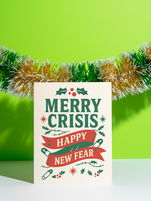 A 5x7 alternative holiday card with a white background and bold, punk-inspired typography. The text reads "Merry Crisis Happy New Fear" in dark green and red. The design features graphic elements like holly, stars, and safety pins, giving it a sarcastic, goth aesthetic. The inside message says "Consider this card your coping mechanism." This snarky, dark humor greeting card is perfect for a funny, unconventional Christmas, capturing a mental health humor and anti-capitalist vibe.