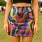 Psychedelic high waisted mini skirt for women featuring a trippy swirl print in yellow, pink, purple, and blue. Fitted bodycon silhouette with 1.5” elastic waistband, made from eco-friendly polyester and spandex blend. Available in sizes S to XL with built-in UPF 50 sun protection and odor-resistant, quick-dry performance fabric. Festival-ready, rave-approved, and styled for bold streetwear and summer outfits.
