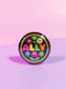 Vibrant ALLY pinback button featuring 70s-style embroidered flowers and lettering in pink, yellow, green, and blue against a black background, surrounded by a rainbow border. A colorful statement accessory combining punk activism and retro flower power aesthetics for backpacks, jackets, and protest wear.