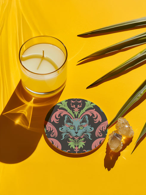 Circular ceramic coaster featuring a turquoise cat face with green eyes on black background, surrounded by pink scrollwork and green leaves in Victorian damask style.