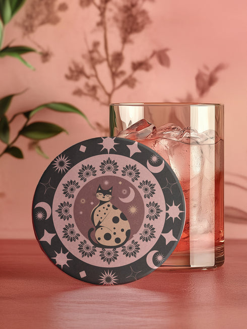 Round ceramic coaster featuring a stylized black cat with polka dots surrounded by pink flowers, moons, and stars on a black background with pink accents