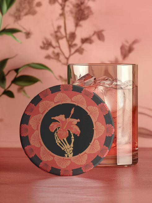 Round ceramic coaster featuring a skeleton hand holding a coral hibiscus flower, surrounded by art deco fan patterns in coral and black