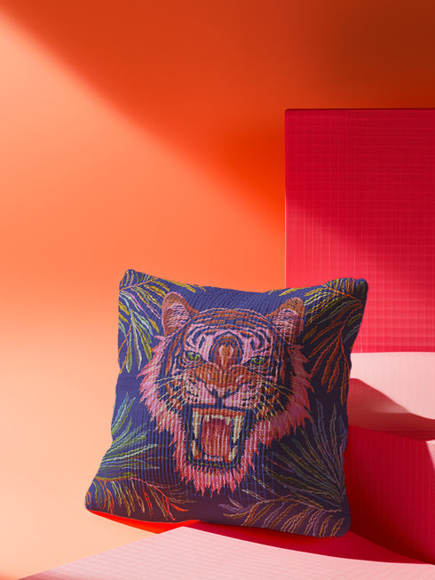 Square woven pillow featuring a fierce pink tiger with bared fangs against electric blue background surrounded by psychedelic jungle leaves. Textured tapestry design creates vibrant maximalist tiger decor perfect for gothic or eclectic home styling.