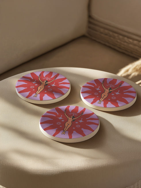 Round ceramic coaster featuring a nude goddess figure holding candles, surrounded by red sunbursts and stars on a lavender background with celestial symbols