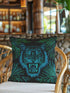 Square woven pillow featuring fierce turquoise tiger with bared fangs against black background surrounded by neon jungle leaves. Textured tapestry creates vibrant midnight tiki decor perfect for rockabilly, maximalist room styling.