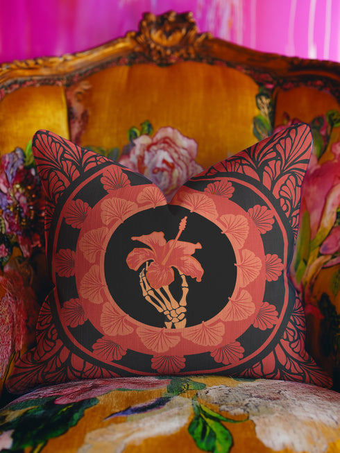 Square pillow cover featuring a golden skeleton hand holding a coral hibiscus flower, surrounded by fan-shaped coral motifs on a black background in an Art Nouveau style.