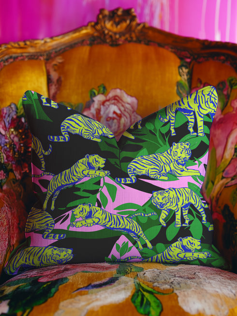 Square pillow cover featuring neon chartreuse tigers with cobalt blue stripes lounging among emerald green palm fronds on a black background with pink geometric accents.