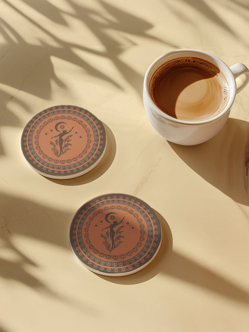 Round ceramic coaster featuring a silhouetted dancing figure reaching for a crescent moon, surrounded by concentric rings of stars and botanical patterns in terracotta and umber tones
