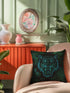 Square woven pillow featuring fierce turquoise tiger with bared fangs against black background surrounded by neon jungle leaves. Textured tapestry creates vibrant midnight tiki decor perfect for rockabilly, maximalist room styling.