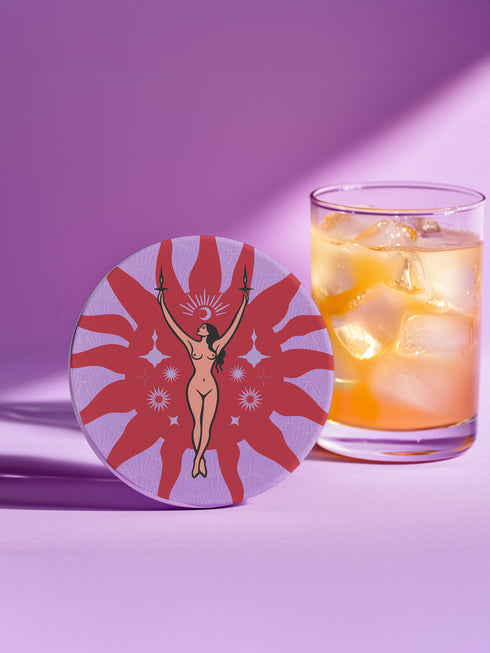 Round ceramic coaster featuring a nude goddess figure holding candles, surrounded by red sunbursts and stars on a lavender background with celestial symbols