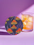 Round ceramic coaster featuring orange and yellow mushrooms with striped caps against a dark background with flowing purple lines in a psychedelic 70s style