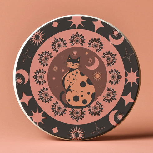Round ceramic coaster featuring a stylized black cat with polka dots surrounded by pink flowers, moons, and stars on a black background with pink accents