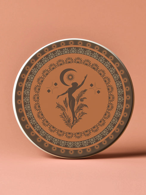 Round ceramic coaster featuring a silhouetted dancing figure reaching for a crescent moon, surrounded by concentric rings of stars and botanical patterns in terracotta and umber tones