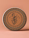 Round ceramic coaster featuring a silhouetted dancing figure reaching for a crescent moon, surrounded by concentric rings of stars and botanical patterns in terracotta and umber tones