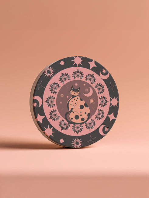 Round ceramic coaster featuring a stylized black cat with polka dots surrounded by pink flowers, moons, and stars on a black background with pink accents