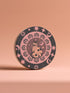 Round ceramic coaster featuring a stylized black cat with polka dots surrounded by pink flowers, moons, and stars on a black background with pink accents