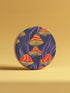 Round ceramic coaster featuring orange and yellow mushrooms with striped caps against a dark background with flowing purple lines in a psychedelic 70s style