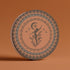 Round ceramic coaster featuring a silhouetted dancing figure reaching for a crescent moon, surrounded by concentric rings of stars and botanical patterns in terracotta and umber tones