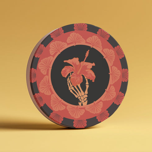Round ceramic coaster featuring a skeleton hand holding a coral hibiscus flower, surrounded by art deco fan patterns in coral and black