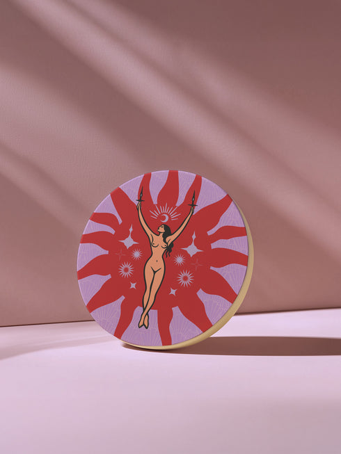 Round ceramic coaster featuring a nude goddess figure holding candles, surrounded by red sunbursts and stars on a lavender background with celestial symbols