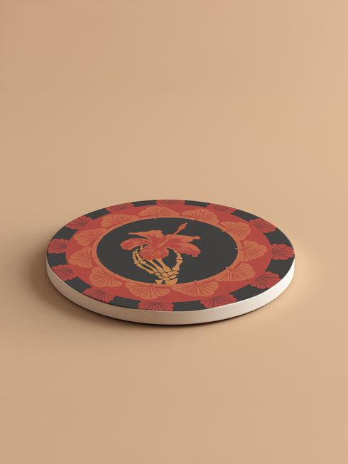Round ceramic coaster featuring a skeleton hand holding a coral hibiscus flower, surrounded by art deco fan patterns in coral and black
