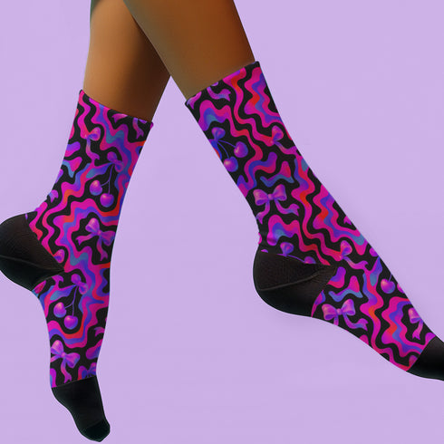 Coquette-style crew socks featuring a bold black background with hot pink and purple psychedelic squiggles, cherries, and shiny pink bows. Made of a soft polyester-spandex blend with reinforced black toe and heel. Fits US women's sizes 5–12 and men's up to 12. Stretchy, colorful, and cute for dopamine dressing.