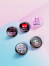 A set of five glossy round pinback buttons with pastel goth and kawaii punk designs, featuring slogans like "Eat The Rich" and "Smash Fascism" in bold pink and black. Each pin has a cute character delivering a powerful message.