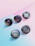 Five glossy 2.25-inch round pinback buttons with pastel punk book-themed designs. Each pin features a different bold phrase like “Read or Die,” “Books Are My Familiar,” and “Give Me Books or Give Me Death,” in pink, purple, and teal colors. Made of tinplate with a safety pin back and glossy scratch-resistant coating.