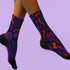 Mid-calf socks with a dark violet-black base featuring a gothic dagger and rose design in gradient shades of red, purple, and pink, with black heels and toes and an illustrated snake detail.