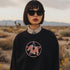 Black sweatshirt featuring a colorful pentagram design with a roller skate in the center, surrounded by dried flowers and set on a textured background.