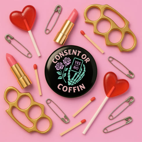 A round black enamel pinback button reading “Consent Or Coffin” in pastel-pink text above and below a mint-green skeleton hand holding a tiny phone interface labeled “YES/NO,” flanked by two stylized pink roses, on a textured purple background.