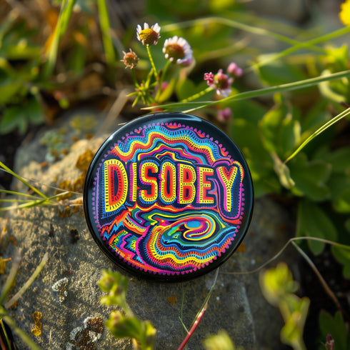 Round black pinback button with neon embroidery-style waves surrounding bold yellow and red "DISOBEY" text.