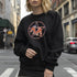 Black sweatshirt featuring a colorful pentagram design with a roller skate in the center, surrounded by dried flowers and set on a textured background.
