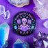 Literary rebel's badge of honor. Black circular button featuring a neon purple skeleton surrounded by floating books and stars. The text 'READ BANNED BOOKS' arcs across the top in bold purple lettering. Perfect for book-loving misfits who devour forbidden knowledge.