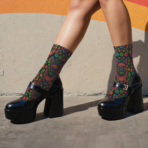 Colorful mid-calf socks with a black background featuring a whimsical folk-art bat pattern in rainbow tones of pink, orange, teal, and green, paired with matching heels and toes.