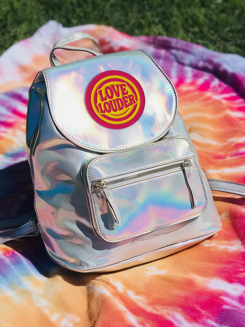 A round, 3-inch embroidered Love Louder patch designed with a vibrant, retro 70s aesthetic. The design features groovy, puffy-style text in a bright, sunny yellow thread, set against a bold magenta pink twill fabric background. The words 'LOVE LOUDER' are stacked to fill the center, encircled by concentric yellow rings that create a hypnotic, radiating effect. The entire circular patch is finished with a clean, durable merrowed border.