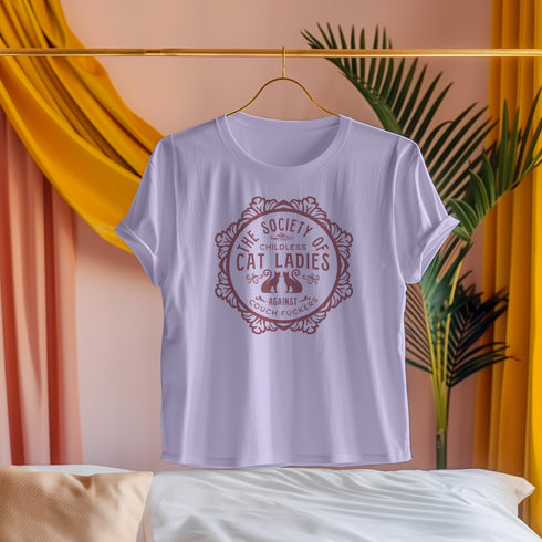 The Society of Childless Cat Ladies Against Couch Fuckers" 2024 election T Shrort design featuring two cats in an ornate circular frame, available in white and purple.