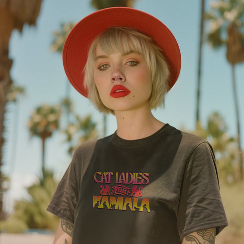 Faded vintage Black t-shirt with "Cat Ladies for Kamala" in retro-style pink and yellow lettering. Cat silhouettes accent the text.