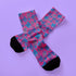Fun and playful socks adorned with vibrant tiger head motifs on a pink background, with black heels and toes, ideal for animal lovers and those who enjoy unique designs