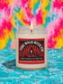 A 9-ounce hand-poured candle inspired by the TV show Twin Peaks, named "Fire Walk With Fir." The candle is made from a creamy, off-white coconut apricot blended wax, housed in a clear glass vessel with a classic, slightly tapered shape. A prominent matte-finish label on the front features the title in a stylized font over a red and black graphic with flame and fir tree motifs. The label also lists scent notes of cypress, lemon peel, fir, amber, and moss.
