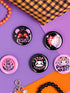 A set of five glossy round pinback buttons with pastel goth and kawaii punk designs, featuring slogans like "Eat The Rich" and "Stop Fascism" in bold pink and black. Each pin has a cute character with a rebellious message.