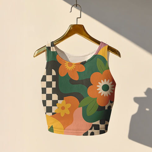 Cropped racerback tank top featuring bold retro floral print with orange and yellow mod flowers, green leaves, black and white checkerboard pattern, and abstract wavy designs. Fitted athletic style crop top in vibrant 70s inspired botanical print with performance fabric construction. Women's festival rave wear cropped camisole with psychedelic flower power design perfect for summer concerts, Y2K fashion looks, and alternative streetwear styling.
