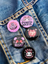 A set of five glossy round pinback buttons with pastel goth and kawaii punk designs, featuring slogans like "Eat The Rich" and "Stop Fascism" in bold pink and black. Each pin has a cute character with a rebellious message.