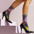 Colorful crew-length socks with a vibrant floral pop-art collage design, featuring abstract roses in yellow, lavender, pink, and orange tones, polka dots, and zebra stripes on a black background.