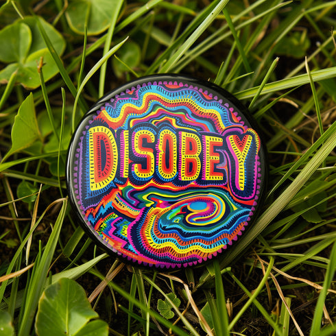 Round black pinback button with neon embroidery-style waves surrounding bold yellow and red "DISOBEY" text.