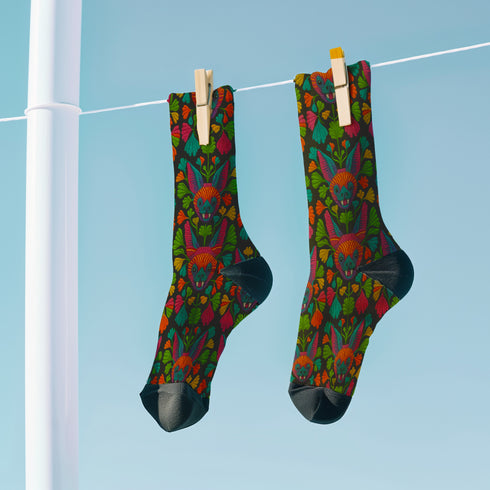 Colorful mid-calf socks with a black background featuring a whimsical folk-art bat pattern in rainbow tones of pink, orange, teal, and green, paired with matching heels and toes.